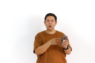 Meraklı bir Asyalı beyaz arka planda cep telefonunu kullanırken kafası karışmış ya da kararsız görünüyor..