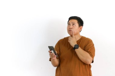 Meraklı bir Asyalı beyaz arka planda cep telefonunu kullanırken kafası karışmış ya da kararsız görünüyor..