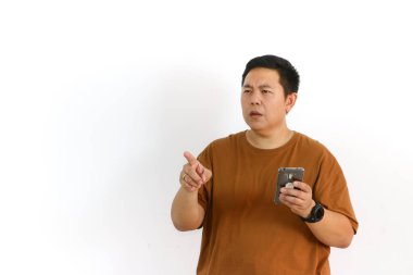 Meraklı bir Asyalı beyaz arka planda cep telefonunu kullanırken kafası karışmış ya da kararsız görünüyor..