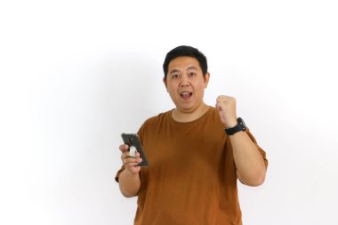 Endonezyalı Asyalı bir adam akıllı bir telefon tutuyor, iyi haber ya da galibiyet hakkında tezahürat yapıyor ve heyecanını dile getiriyor..