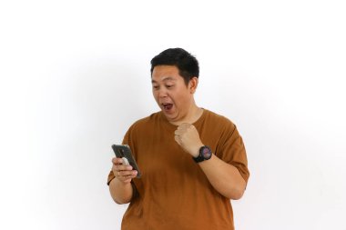 Asyalı bir erkek, akıllı telefon kullanırken kazanan bir hareketle tepki veriyor ve yüz ifadesi heyecanlanıyor..