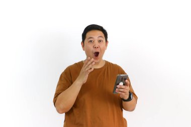 Asyalı bir erkek, akıllı telefon kullanırken kazanan bir hareketle tepki veriyor ve yüz ifadesi heyecanlanıyor..