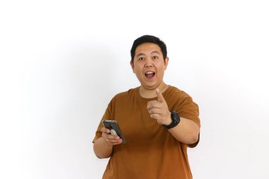 Asyalı bir erkek, akıllı telefon kullanırken kazanan bir hareketle tepki veriyor ve yüz ifadesi heyecanlanıyor..