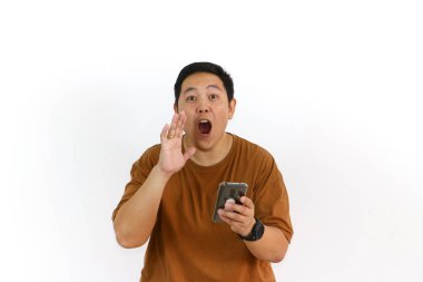 Endonezyalı bir Asyalı beyaz arka planda akıllı telefonunu tutarken avucunun içine bağırıyor..