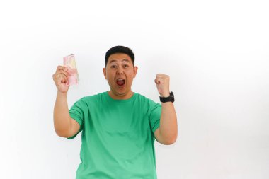 Heyecanlı Asyalı adam elinde Endonezya Rupiah banknotları, ağzı açık ve gözleri açık stüdyodaki başarısını alkışlıyor..