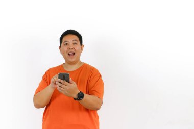 Siyah tişörtün üzerine günlük turuncu tişört giyen 40 'lı yaşlardaki yakışıklı erkek manken bir cep telefonu tutuyor, mesajları kontrol ediyor veya internette olumlu bir şekilde geziniyor..