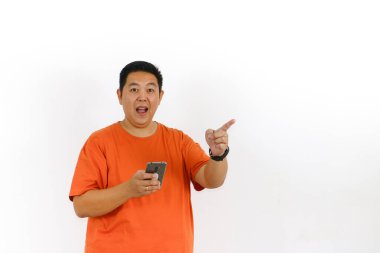 Turuncu tişörtlü heyecanlı adam akıllı telefonunu kullanarak mutlu bir şekilde parmağını kaldırırken parlak bir fikir buluyor..