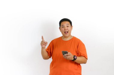 Turuncu tişörtlü heyecanlı adam akıllı telefonunu kullanarak mutlu bir şekilde parmağını kaldırırken parlak bir fikir buluyor..