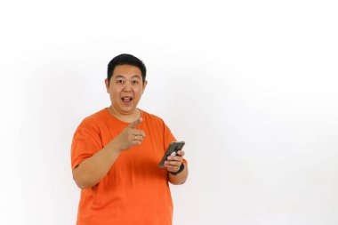 Turuncu tişörtlü heyecanlı adam akıllı telefonunu kullanarak mutlu bir şekilde parmağını kaldırırken parlak bir fikir buluyor..