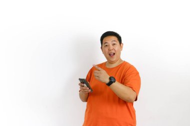 Turuncu tişörtlü heyecanlı adam akıllı telefonunu kullanarak mutlu bir şekilde parmağını kaldırırken parlak bir fikir buluyor..