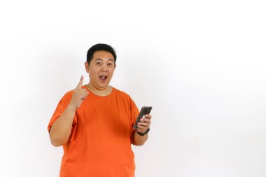 Turuncu tişörtlü heyecanlı adam akıllı telefonunu kullanarak mutlu bir şekilde parmağını kaldırırken parlak bir fikir buluyor..