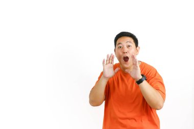 Turuncu tişörtlü şaşkın Asyalı adam ağzı açık şekilde tepki veriyor ve ellerini kaldırıyor. Tamamen güvensizlik ve şok olduğunu ifade ediyor..