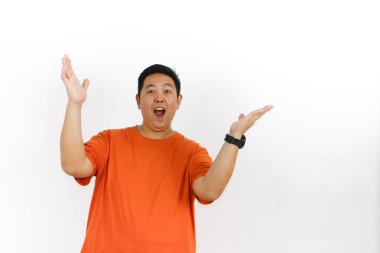 Turuncu tişörtlü şaşkın Asyalı adam ağzı açık şekilde tepki veriyor ve ellerini kaldırıyor. Tamamen güvensizlik ve şok olduğunu ifade ediyor..