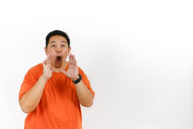 Turuncu tişörtlü şaşkın Asyalı adam ağzı açık şekilde tepki veriyor ve ellerini kaldırıyor. Tamamen güvensizlik ve şok olduğunu ifade ediyor..