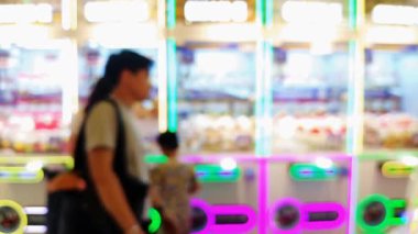 Işıl ışıl ışıkları olan kalabalık eğlence merkezinin bulanık arka planı ve pençe makinelerinden ödül kazanmaya çalışan insanlar..