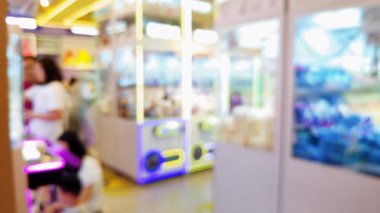 Işıl ışıl ışıkları olan kalabalık eğlence merkezinin bulanık arka planı ve pençe makinelerinden ödül kazanmaya çalışan insanlar..