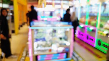 Canlı bir oyun salonunun içini ön plan pençe makineleri ve sıcak, parlak ışıklarla bulanıklaştırdı..