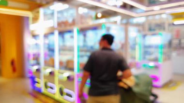 Canlı bir oyun salonunun içini ön plan pençe makineleri ve sıcak, parlak ışıklarla bulanıklaştırdı..