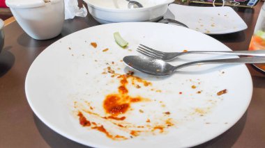 Kalan yemek artıkları metal çatal ve kaşık ile bir kaşık kirli tabakta bir kafe masasında.