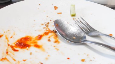 Kalan yemek artıkları metal çatal ve kaşık ile bir kaşık kirli tabakta bir kafe masasında.