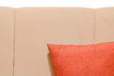 Tarafsız bej bir yatak başlığına yaslanmış canlı kırmızı bir yastığın yakın plan çekimi..