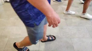 Kalabalık bir alışveriş merkezinin parlak seramik zemininde yürüyor..