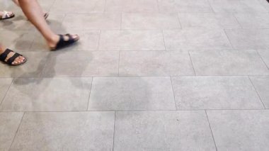 Kalabalık bir alışveriş merkezinin parlak seramik zemininde yürüyor..