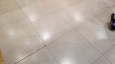 Kalabalık bir alışveriş merkezinin parlak seramik zemininde yürüyor..