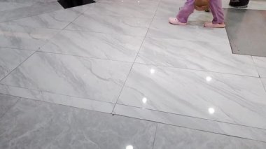 Kalabalık bir alışveriş merkezinin parlak seramik zemininde yürüyor..