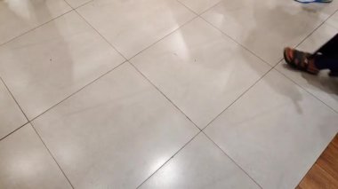 Kalabalık bir alışveriş merkezinin parlak seramik zemininde yürüyor..
