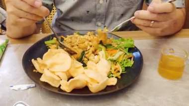 Asyalı bir adam öğle yemeği için çatal ve kaşık kullanarak lezzetli kızarmış pirinç şehriyesiyle tavuğu karıştırıyor..