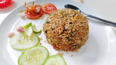 Taze kesilmiş salatalık ve domatesle servis edilen bir tabak otantik Endonezya usulü kızarmış pirinç.