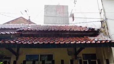 Kasvetli bir öğleden sonra, banliyö evlerinin geleneksel kil kiremit çatılarına yağmur suyu yağıyor.