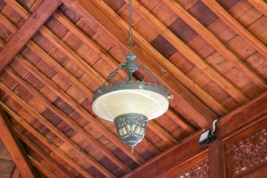 Süslü metal bir kafesi ve ahşap tavanda buzlu cam kasesi olan antika bir kolye.