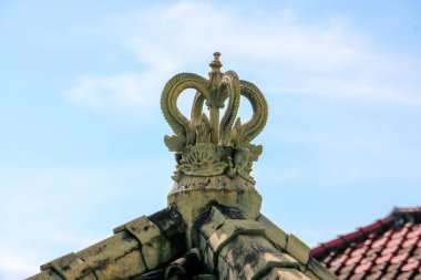 Ancient stone roof finial with intricate crown carvings on a traditional Javanese house