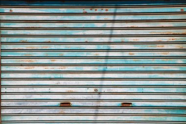 Yıpranmış mavi metal bir kepenk ve birkaç parça kahverengi pas.