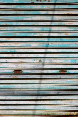 Yıpranmış mavi metal bir kepenk ve birkaç parça kahverengi pas.