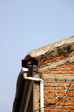 Kırsal açıkta kırmızı tuğla duvar, açık mavi gökyüzünün altında dikey beyaz plastik yağmur suyu içeriyor.