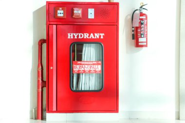 Açık kırmızı bir yangın musluğu ve yangın söndürücü Denpasar 'da 7 Mayıs 2025' te beyaz bir duvara asılmış.