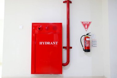 Açık kırmızı bir yangın musluğu ve yangın söndürücü Denpasar 'da 7 Mayıs 2025' te beyaz bir duvara asılmış.