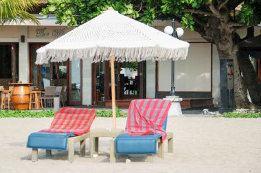 Bali 'deki beyaz makrome şemsiyelerin altında rahat, mavi koltukları olan plaj kurulumu.