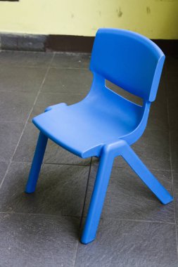 Çocuklar için tasarlanmış küçük mavi bir plastik sandalye bir oyun odasında ya da okulda oturur.