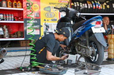 Profesyonel motosiklet tamircisi, 9 Kasım 2025 'te Bali' deki Planet Ban hizmet merkezinde mavi bir scooter tamir ediyor.