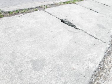 Yukarıdan bakıldığında, kaldırımda küçük dikdörtgen saplı delikleri olan gri beton drenaj kapağı görülüyor.