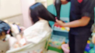 Annelerin ve çocukların saç bakım hizmetlerinden hoşlandığı canlı bir salon ortamının odaklı olmayan görüntüleri.