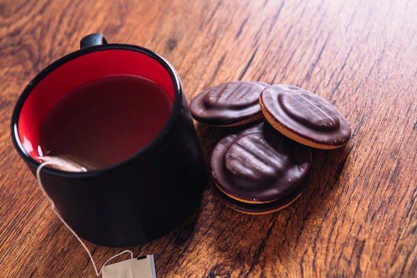 Muchas galletas con chispas de chocolate y una taza de té sobre fondo de madera — Foto de Stock