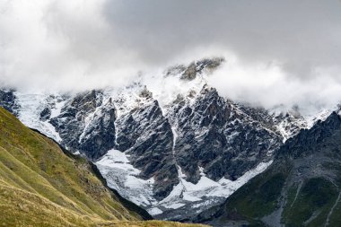 Ushguli Gürcistan yakınlarındaki Kafkasya Dağları 'ndaki Shkhara Buzulu: Engebeli tepeleri, kayaları ve sisli gökyüzü olan görkemli Alp manzarası. Yüksek kalite fotoğraf