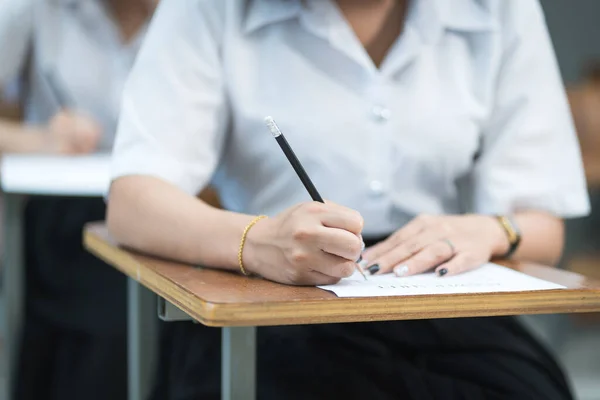 Close up of young university students concentrate on doing examination in classroom. Girl student writes on the examinations answer paper in the classroom.