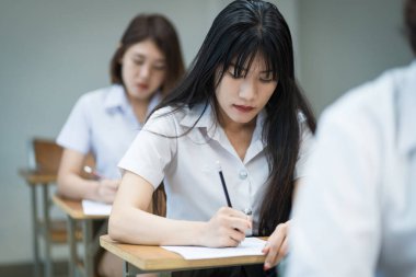 Genç üniversite öğrencilerinin seçici odak noktası ders koltuklarında oturup final sınavı yapmak ve sınav kağıdına cevap kağıtları yazmak. Üniformalı üniversite öğrencileri sınıfta..