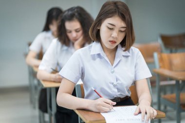 Genç üniversite öğrencilerinin seçici odak noktası ders koltuklarında oturup final sınavı yapmak ve sınav kağıdına cevap kağıtları yazmak. Üniformalı üniversite öğrencileri sınıfta..